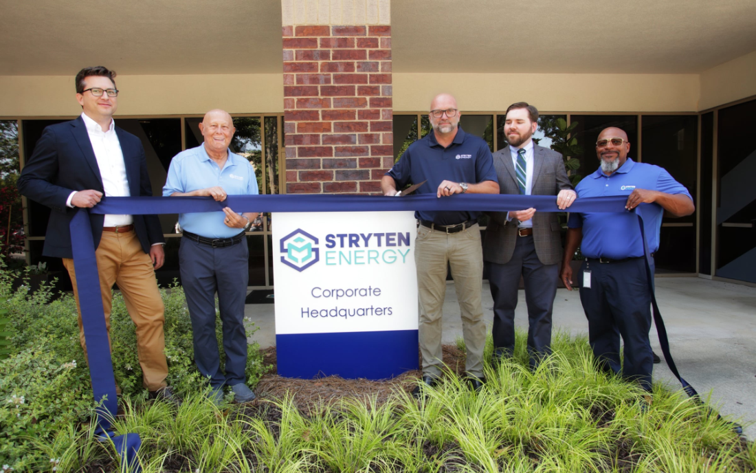 five men holding a blue ribbon, one about to cut it