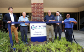 five men holding a blue ribbon, one about to cut it